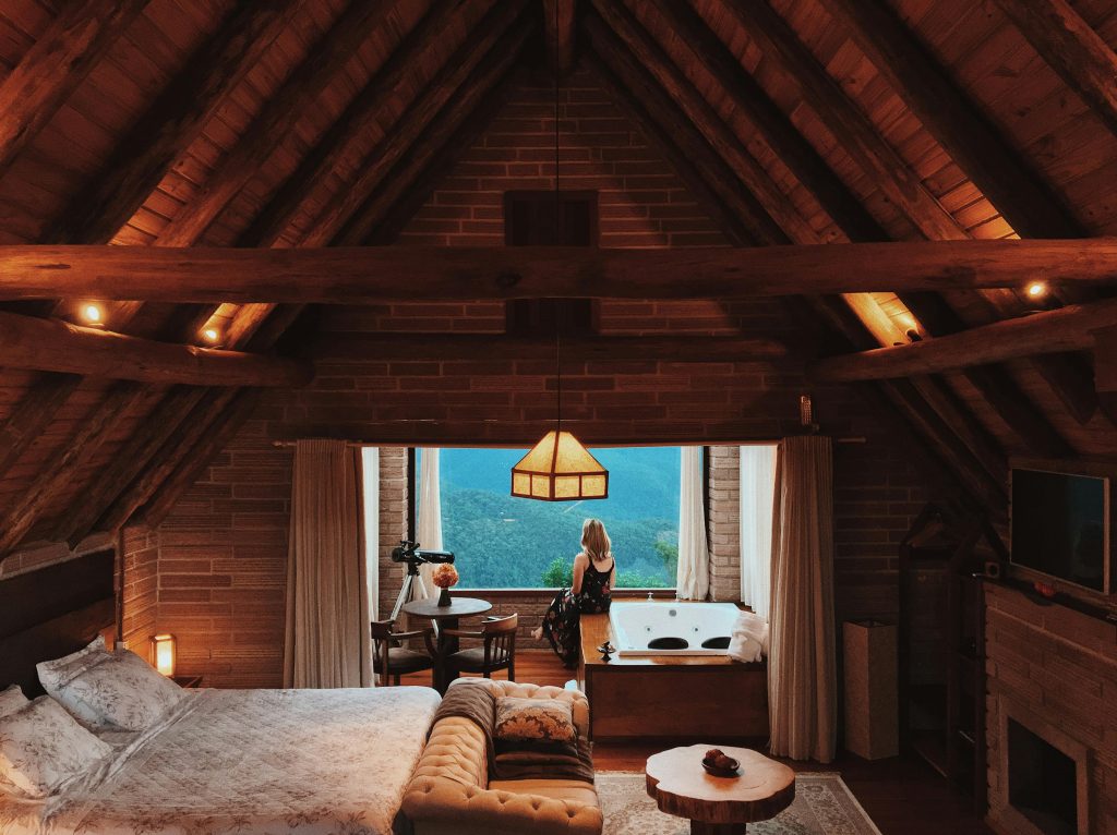 Rustic attic hotel room with exposed wooden beams, cozy bed, and private Jacuzzi tub by panoramic window